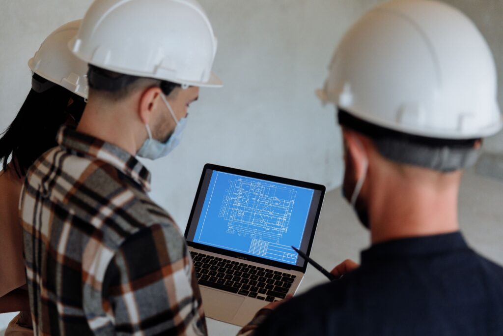 Contractors in hard hats reviewing a blueprint on a laptop together